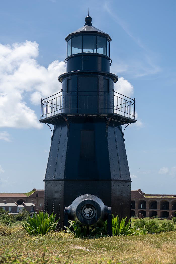 A historic black lighthouse stands tall at Fort Jefferson, Key West, against a blue sky.